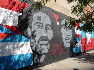 Stylised mural with images of Pedro Albizu Campos and Ernesto 'Che' Guevara blending into Puerto Rican and Cuban flags respectively, on a wall in Spanish Harlem
